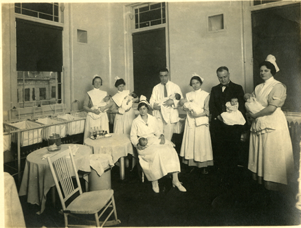 Doctors and nurses, c. 1919, hold newborns in the maternity ward nursery.