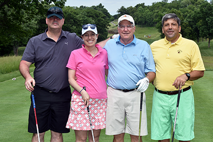 A group of three men and one woman posing for a photo on the golf course