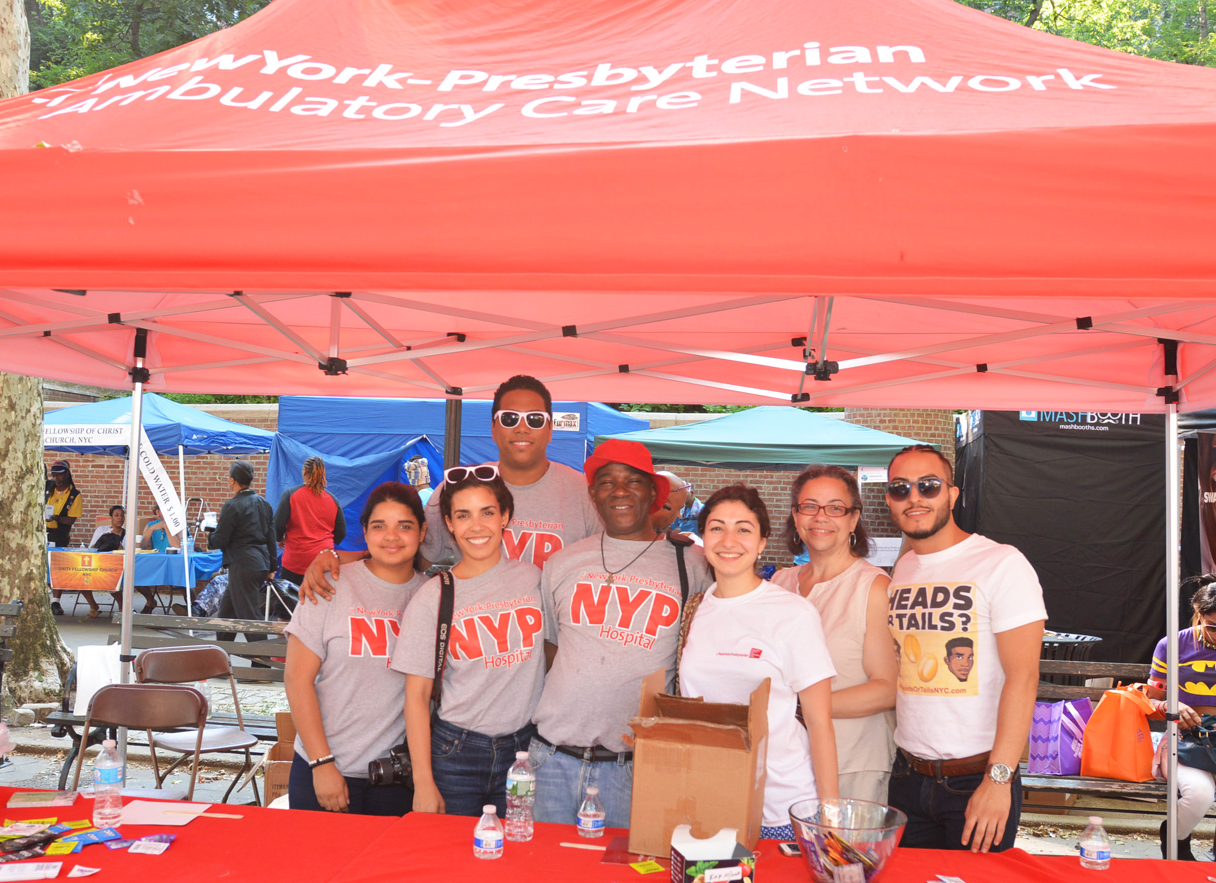 A group of poeple posing for a photo under the NewYork-Presbyterian booth at the Harlem pride event