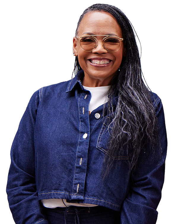 Smiling African American woman wearing gold-rimmed glasses, a white top, and a cropped dark denim jacket. She has long, straight dark hair swept to one side.