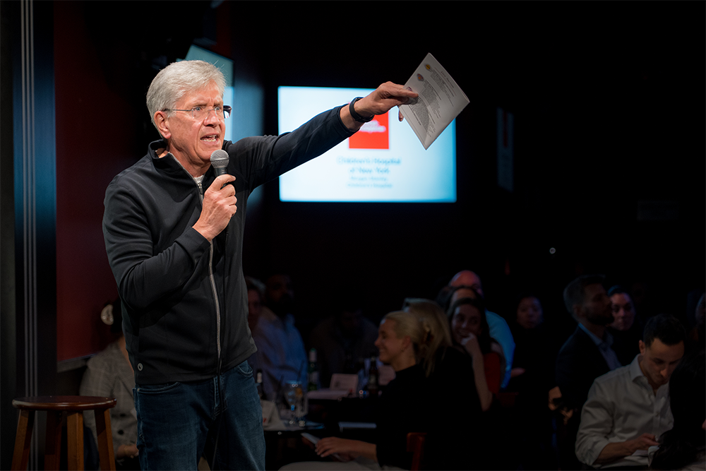 A man with a microphone, gesturing with a piece of paper.