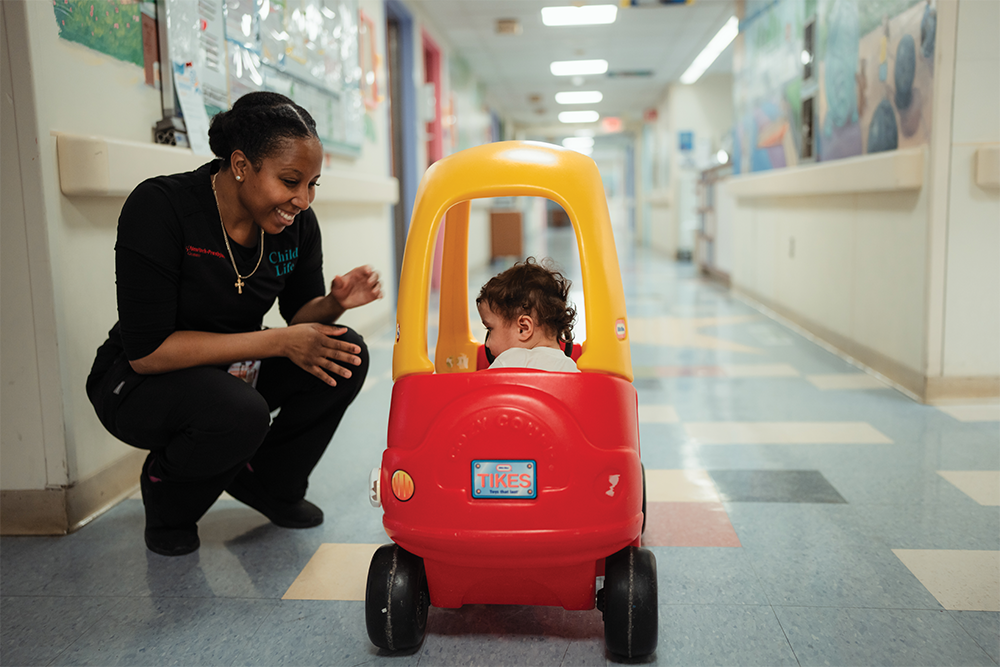 Doctor squating with a child in a play car.
