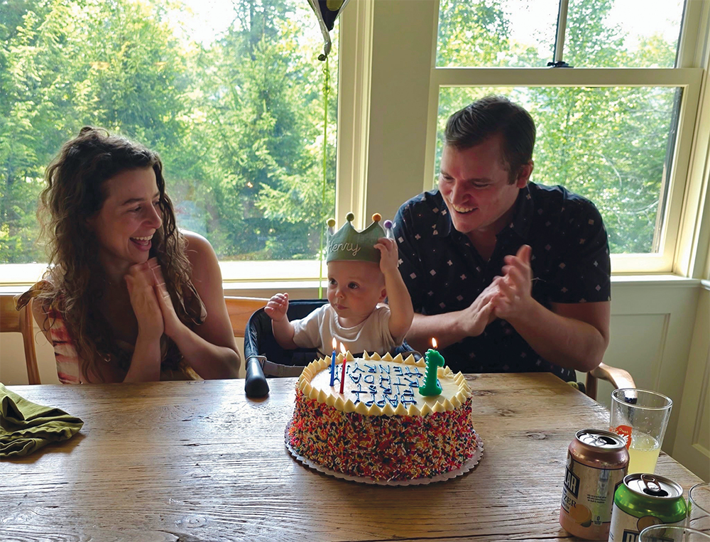 Parents with baby at a table with a birthday cake.