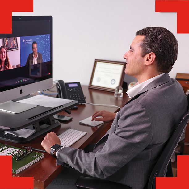 A man in a suit, on a video conference call at a desk.