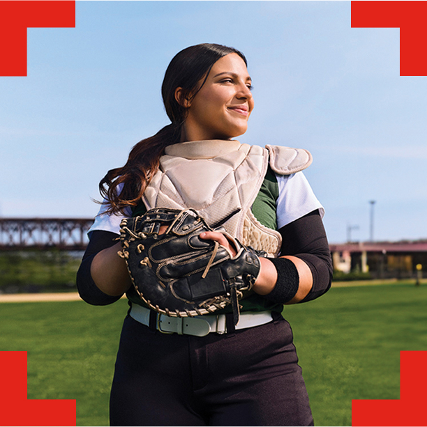 A young woman in a softball uniform and catcher's equipment.