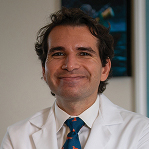 Man smiling in blue tie and lab coat.