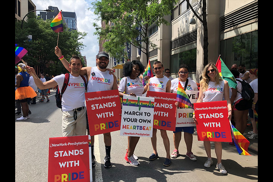 Six people holding up NewYork-Presbyterian signs and flags LGBTQ pride event 