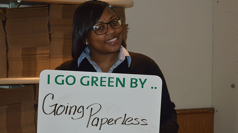 A woman holding a sign that say I go green by... going paperless!