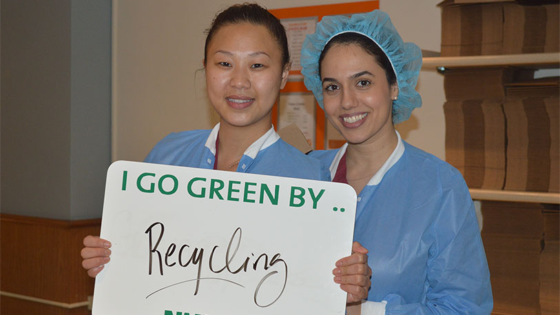 Two women holding a sign that says I go green by... recycling