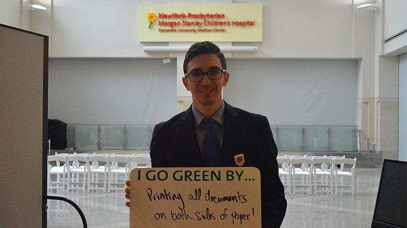 A man holding a sign that say I go green by... printing all documents on both sides of paper