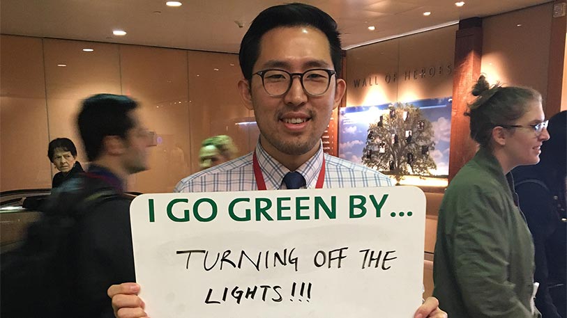 A man holding a sign that say I go green by... turning off the lights