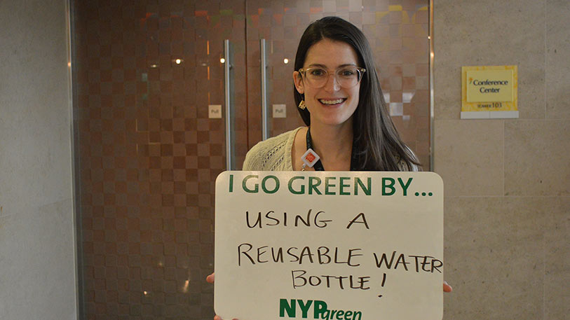 A woman holding a sign that say I go green by... using a reusable water bottle!