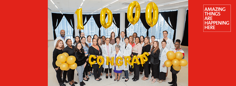 A group of healthcare professionals posing for a photo with balloons that read 1000 Congrats
