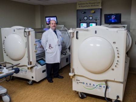 A doctor standing next to two hyperbaric chambers