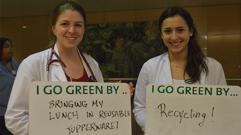 Two women holding signs that say I go green by... bringing my lunch to work and I go green by... recycling