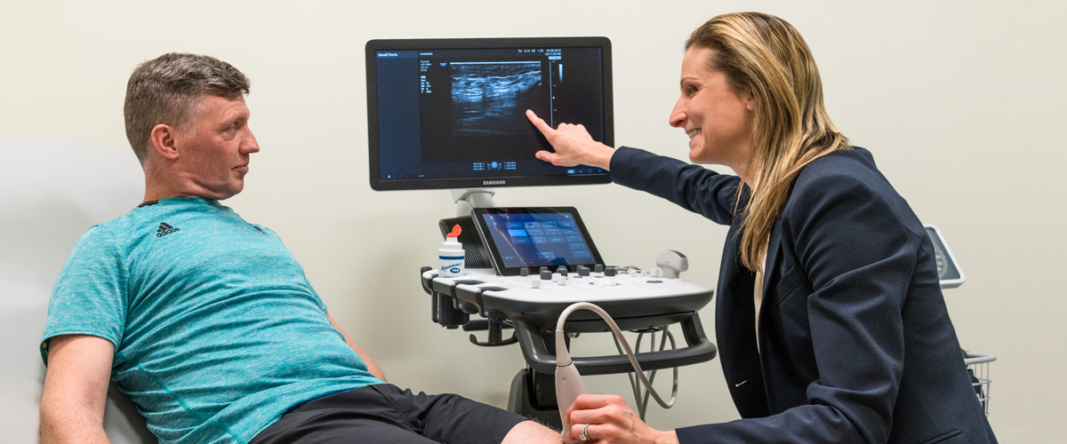 A healthcare provider examining a patient's knee and pointing to an image on a computer screen
