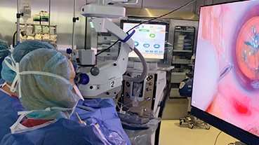 image of doctors and nurses in an operating room looking at a monitor during eye surgery