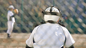image of the back of a baseball catchrer through a fence with pitcher blurred in the background