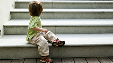 image of a toddler sitting on the stairs with back turned away towards camera