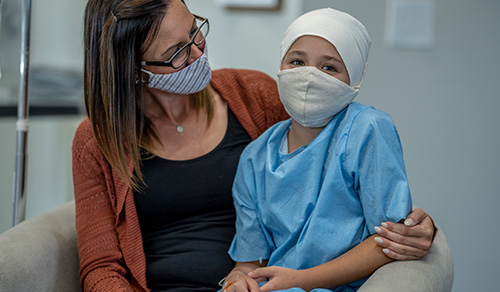 image of masked mom holding and hugging masked teenager cancer patient
