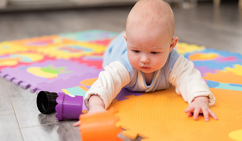 image of infant crawling on foam mat playing with cups