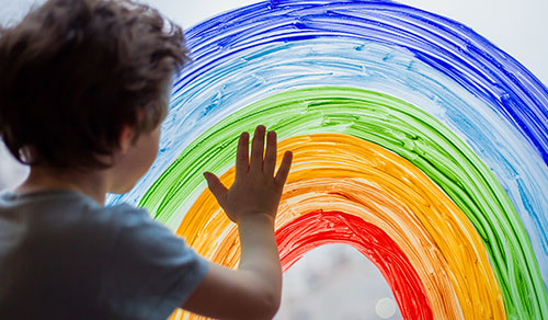 image of kid finger-painting a rainbow on a window
