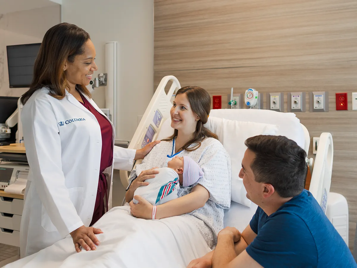 Doctor checking in on a mother and father with their newborn