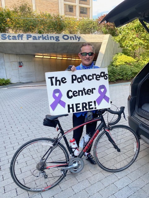 Dr. Chabot standing next to a bike holding a sign that says Pancreas Center Here