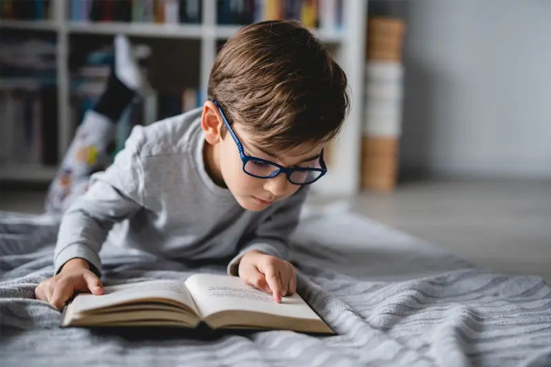 A child with glasses reading a book.