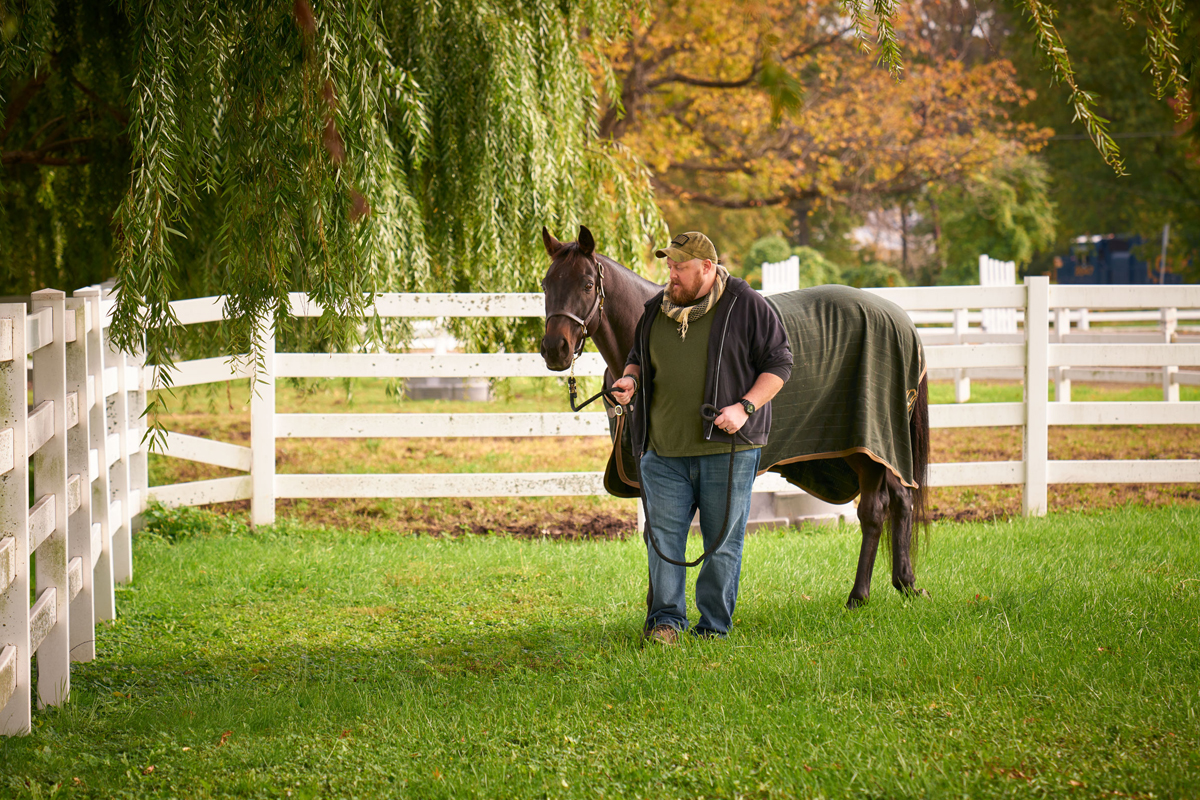 A man leading a horse around the pasture.