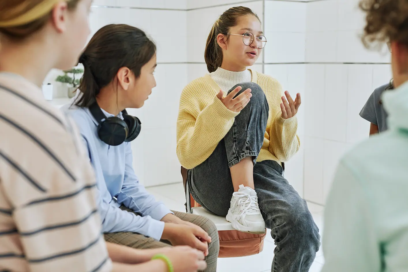 Girl casually sitting on a chair addressing a group of teen