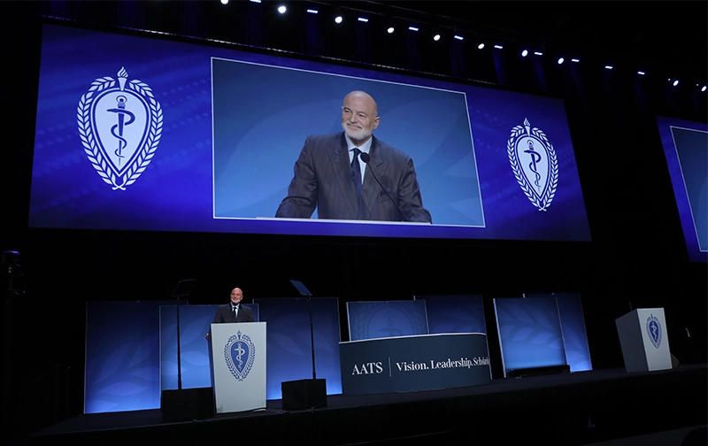 Dr. Emile Bacha at podium with giant projection screen above him at AATS 2026.